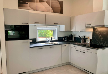 Moderne keuken in chalet met witte kasten, zwart aanrechtblad en raam met uitzicht op natuur.