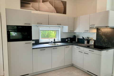Moderne keuken in chalet met witte kasten, zwart aanrechtblad en raam met uitzicht op natuur.