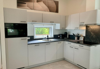 Cucina moderna in uno chalet con mobili bianchi, piano nero e finestra con vista sul verde.