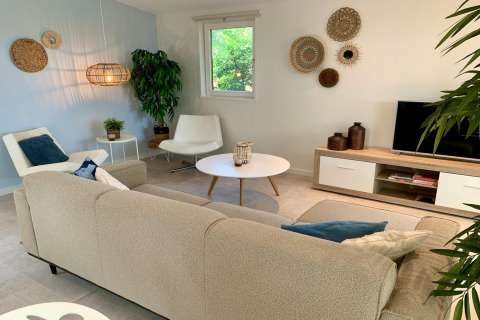Salón de chalet moderno con sofá beige, sillones blancos y decoración natural en los Países Bajos.