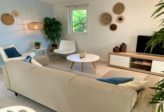 Woonkamer in modern chalet met beige bank, witte stoelen en natuurlijke decoratie in Nederland.