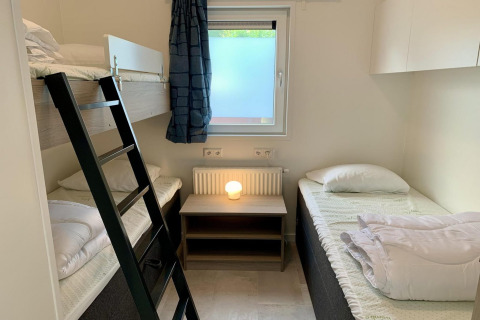 Modern chalet met stapelbed, enkel bed, nachtkastje en raam in Nederland.