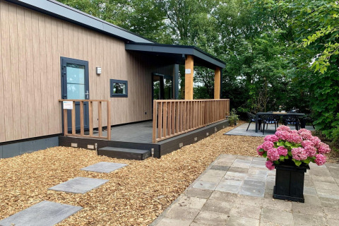 Chalet moderno nei Paesi Bassi con terrazza in legno, veranda e fiori davanti immersi nel verde.