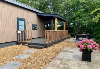 Modern chalet met terras en veranda, omringd door groen, met bloemen in de voorgrond in Nederland.