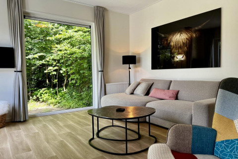 Salon de chalet avec grande fenêtre donnant sur le jardin, canapé moderne, œuvre murale et table basse ronde.