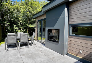 Terrasse extérieure moderne avec table à manger et chaises d'un chalet élégant entouré d’arbres verdoyants.