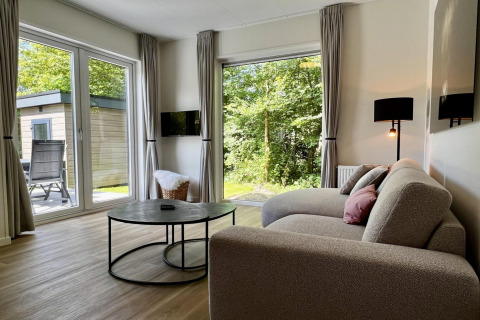 Soggiorno di un unico chalet per 5 persone con divano moderno, grandi finestre e vista sul giardino in Olanda.