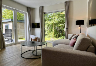 Woonkamer in uniek chalet voor vijf personen met moderne bank, grote ramen en tuinzicht in Nederland.
