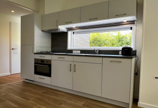 Moderne keuken in een uniek chalet in Nederland, met lichte kasten, oven en groot raam.