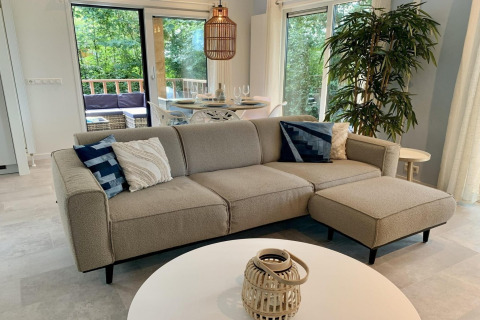 Intérieur de chalet moderne aux Pays-Bas avec canapé beige, coussins bleus et vue sur la terrasse.