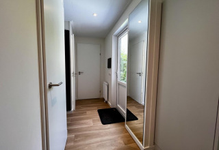 Ingresso luminoso e moderno di uno chalet nei Paesi Bassi con pavimento in legno e grande specchio.