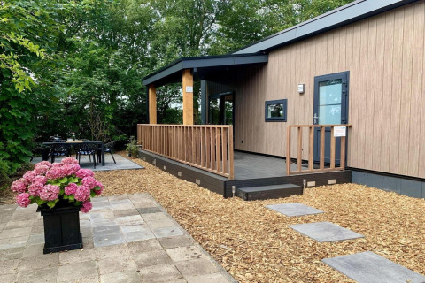 Modern chalet met houten terras, overdekte veranda, tuin en buiteneethoek in Nederland.