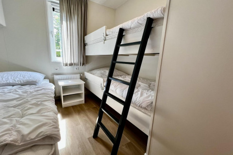 Dormitorio en un chalet holandés con literas, cama individual, ventana y suelo de madera laminada.