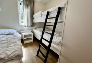 Dormitorio en un chalet holandés con literas, cama individual, ventana y suelo de madera laminada.