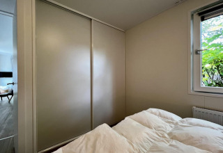 Slaapkamer in chalet in Nederland met kast, raam met tuinzicht en bed met wit dekbed zichtbaar.