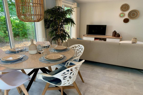 Interno di chalet moderno nei Paesi Bassi con tavolo da pranzo, divano, TV e ampia finestra luminosa.