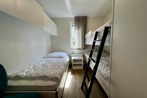 Slaapkamer bij Unique chalet voor 5 met eenpersoonsbed, stapelbed, raam en licht gordijn in Nederland.