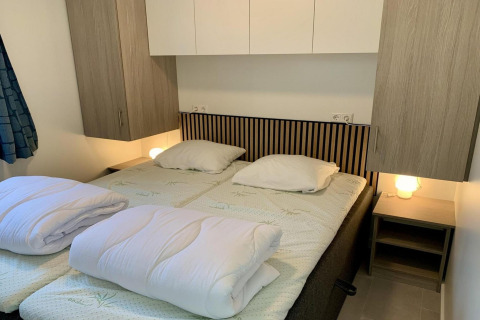 Moderne chalet slaapkamer in Nederland met twee eenpersoonsbedden, houten kasten en lampjes.