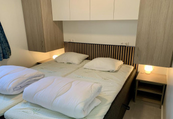 Moderne chalet slaapkamer in Nederland met twee eenpersoonsbedden, houten kasten en lampjes.