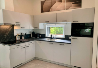 Moderne keuken met witte kasten, zwart aanrecht, raam en apparatuur in een Nederlands chalet.