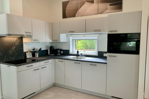 Cuisine moderne avec placards blancs, plan noir, fenêtre et électroménagers dans un chalet aux Pays-Bas.