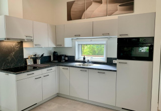 Cuisine moderne avec placards blancs, plan noir, fenêtre et électroménagers dans un chalet aux Pays-Bas.