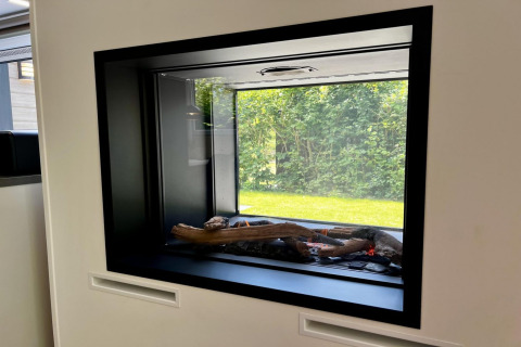 Moderne glazen haard met houtblokken en uitzicht op tuin in ‘Unique chalet for 5 with garden’, Nederland.