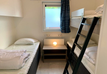 Moderne chaletkamer met stapelbed, eenpersoonsbedden, raam en nachtkastlamp in Nederland.