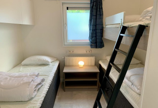 Moderne chaletkamer met stapelbed, eenpersoonsbedden, raam en nachtkastlamp in Nederland.