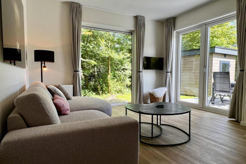 Lichte woonkamer van uniek chalet met moderne bank, ronde tafel en tuinzicht in Nederland.