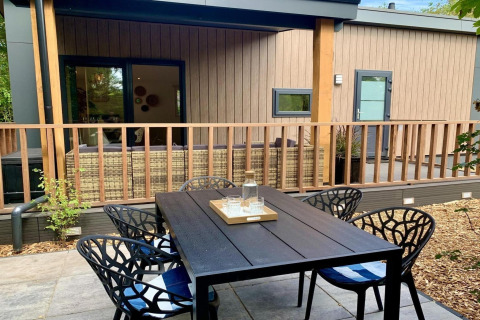 Modern chalet in Nederland met houten terras, veranda, buiteneettafel en stijlvolle stoelen.