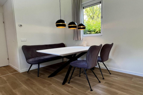 Sala da pranzo moderna con panca nera, due sedie, tavolo bianco e lampade sospese in chalet olandese unico.