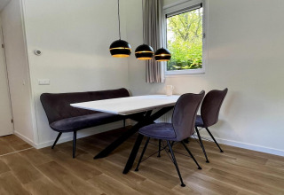 Sala da pranzo moderna con panca nera, due sedie, tavolo bianco e lampade sospese in chalet olandese unico.