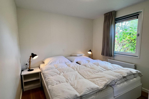 Camera da letto con letto matrimoniale, piumoni bianchi, lampade da comodino e finestra sul giardino.