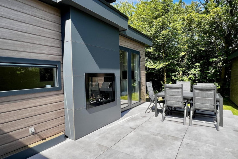 Terrasse moderne de chalet aux Pays-Bas avec table extérieure, chaises, cheminée et jardin verdoyant.