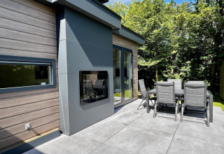 Terraza moderna de chalet en Países Bajos con comedor exterior, chimenea y vistas al jardín verde.