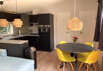 Modern chalet met tuin en terras, eetruimte met gele stoelen en open keuken, gelegen in Nederland.