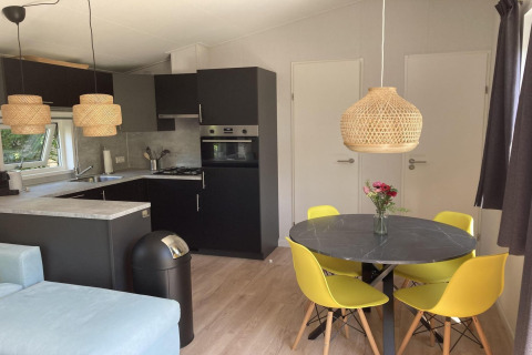 Modern chalet met tuin en terras, eetruimte met gele stoelen en open keuken, gelegen in Nederland.