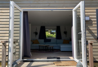 Chalet moderne aux Pays-Bas avec portes vitrées ouvertes donnant sur terrasse et salon confortable.