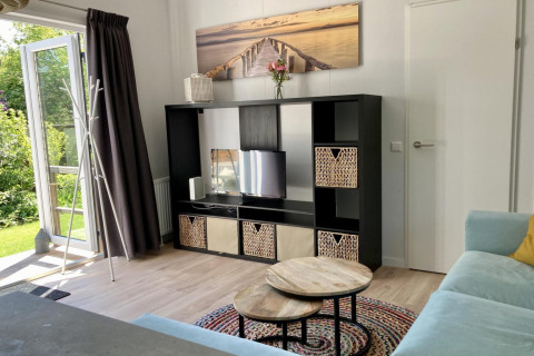 Salón de chalet moderno en Países Bajos con estantería negra, mesas redondas, sofá y puerta al jardín.