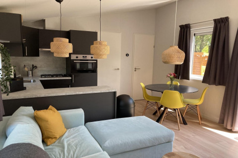 Intérieur de chalet moderne aux Pays-Bas avec cuisine ouverte, chaises jaunes et table ronde.
