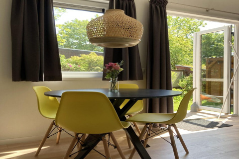 Chalet moderno con jardín y terraza en Países Bajos, comedor con sillas amarillas y flores en la mesa.