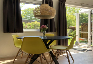 Modernes Chalet mit Garten und Terrasse in den Niederlanden, Essbereich mit gelben Stühlen und Blumen.