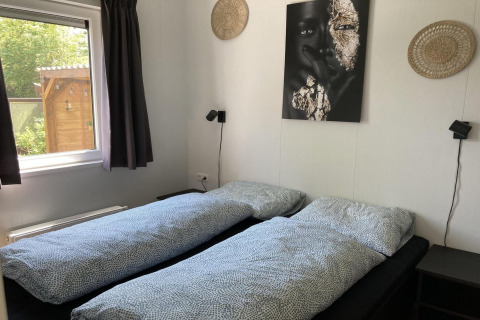 Dormitorio de chalet moderno con dos camas individuales, arte en la pared y vista al jardín en los Países Bajos.