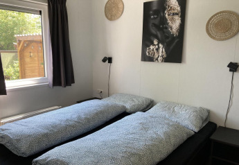 Modern chalet bedroom with two single beds, wall art, natural light, and garden view in the Netherlands.