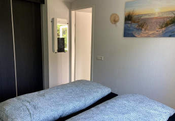 Bright bedroom in a modern chalet featuring two beds, a mirror, closet, and wall art in the Netherlands.