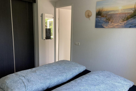 Helles Schlafzimmer im modernen Chalet mit zwei Betten, Spiegel, Schrank und Wandbild in den Niederlanden.