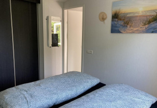 Dormitorio luminoso en un chalet moderno con dos camas, espejo, armario y cuadro en los Países Bajos.