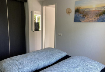 Bright bedroom in a modern chalet featuring two beds, a mirror, closet, and wall art in the Netherlands.