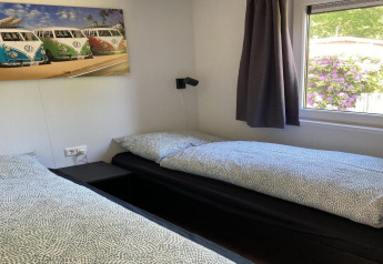 Due letti singoli in uno chalet moderno con finestra, tende e quadro di furgoni VW nei Paesi Bassi.